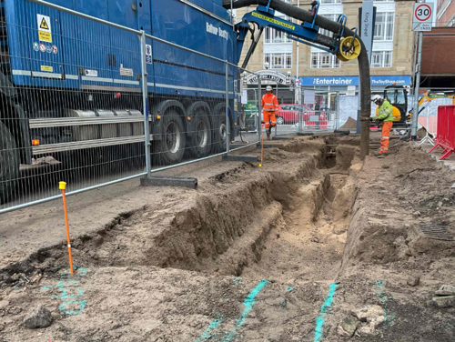 A progress picture of King Street, a large vehicle is pouring concrete into a dug out pit where the pavement was. - February 2025
