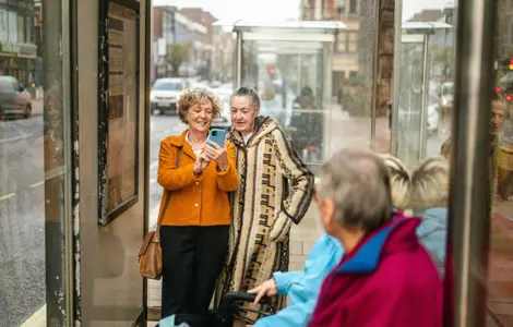Two people looking at phone at bus stop