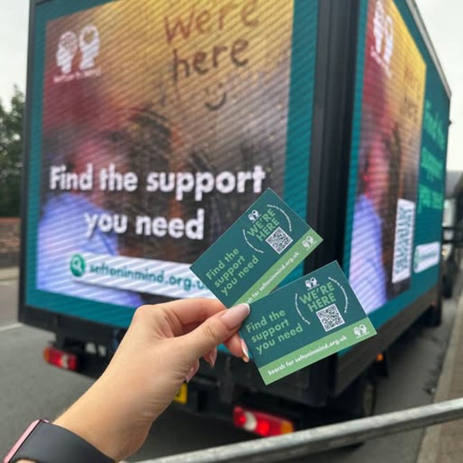 A person holds two green cards that say "We're here. Find the support you need. Search for seftonmind.org.uk" in front