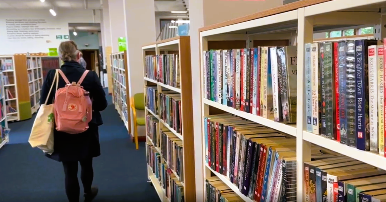 A person walking in Crosby library with a shelves full of books on their right