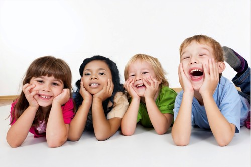Picture of four children laying down with their head in their hands, smiling happily.