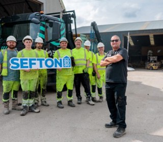 A group of seven workers in high-visibility clothing stand in front of a truck. Six hold a sign that reads SEFTON 2030.