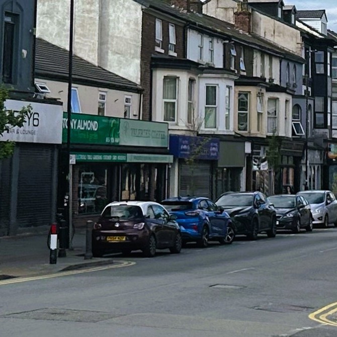 A row of shops with cars parked in front.